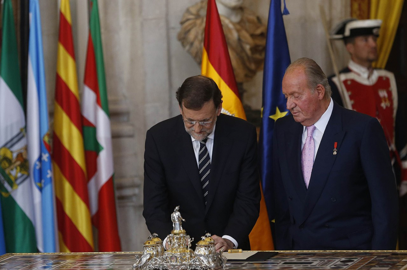 Juan Carlos I next to prime minister Mariano Rajoy, who is seen countersigning the organic law for abdication (18 June 2014). - Photo: https://en.wikipedia.org/