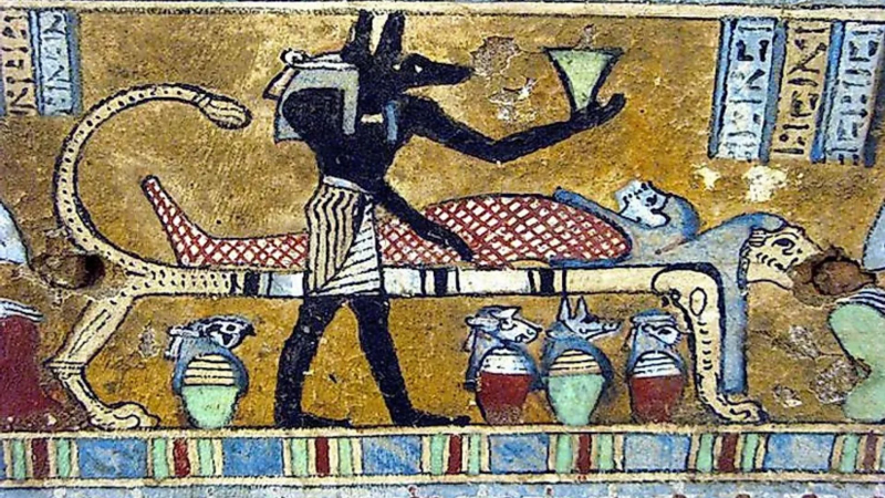 Anubis, the Egyptian God associated with mummification and afterlife is depicted in a painting with the body of the deceased. - worldatlas.com